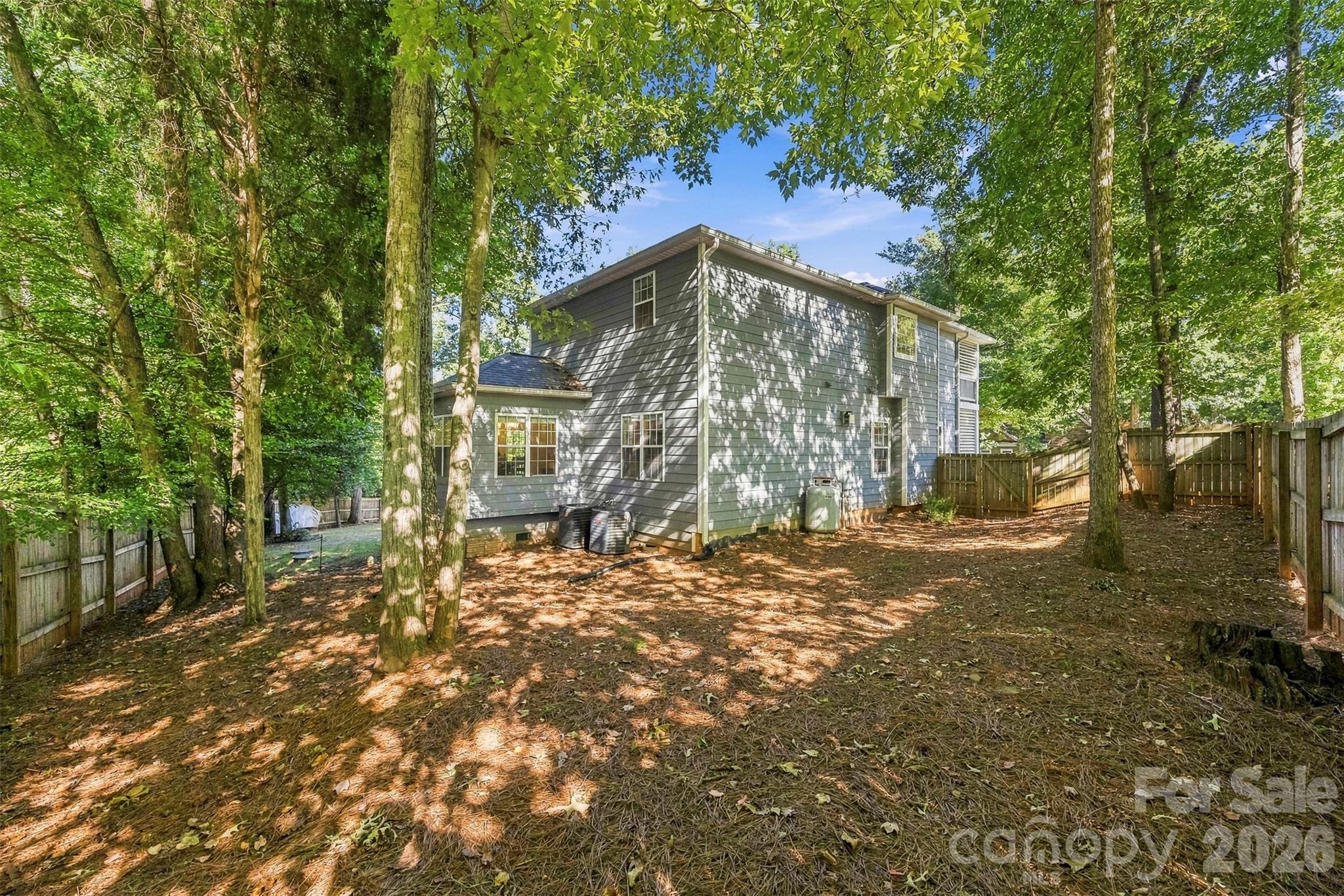 Rear of a gray two-story house in a fenced, tree-shaded backyard.
