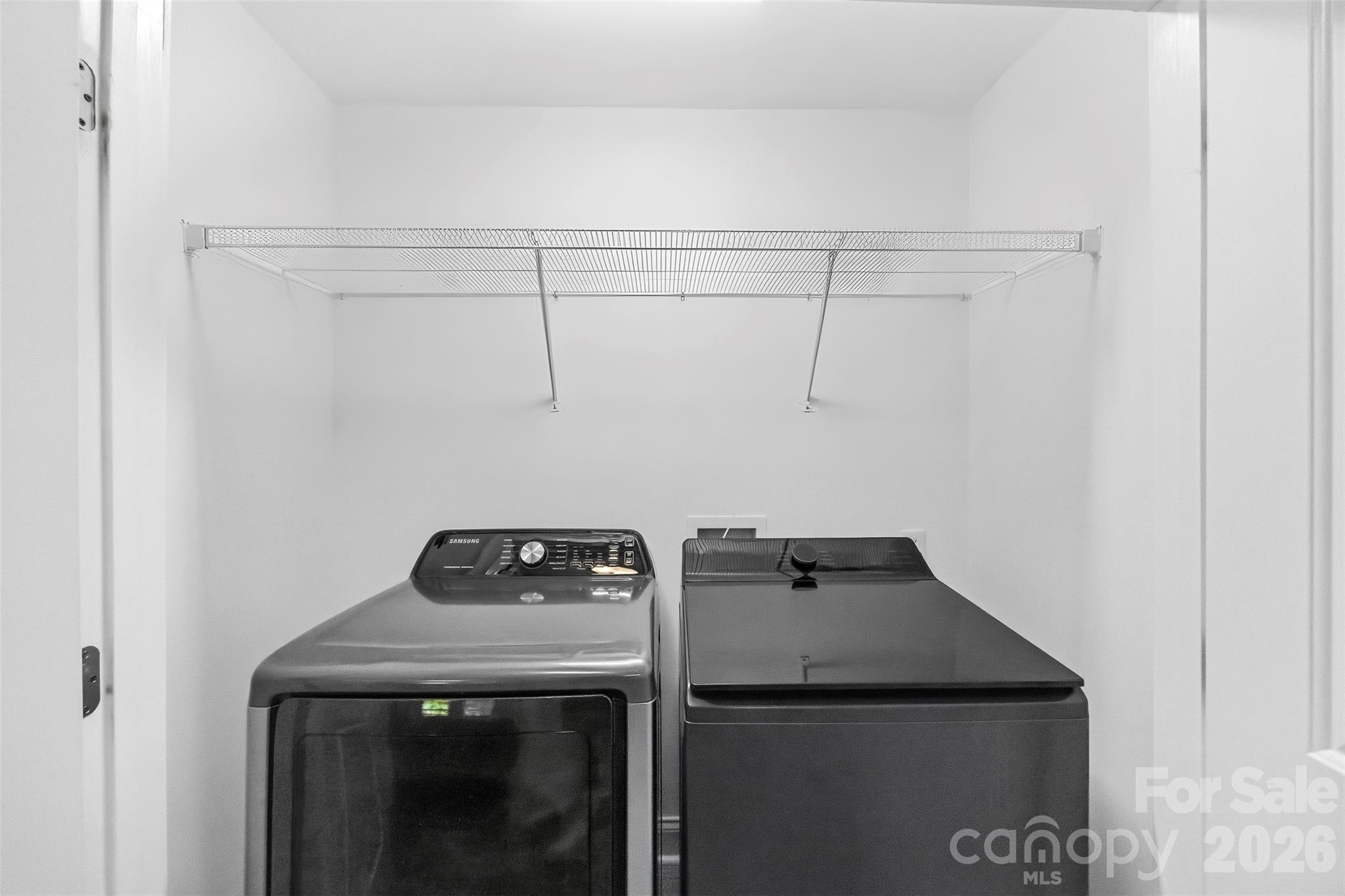 Laundry room with a Samsung dryer and top-loading washer beneath a wide wire shelf.