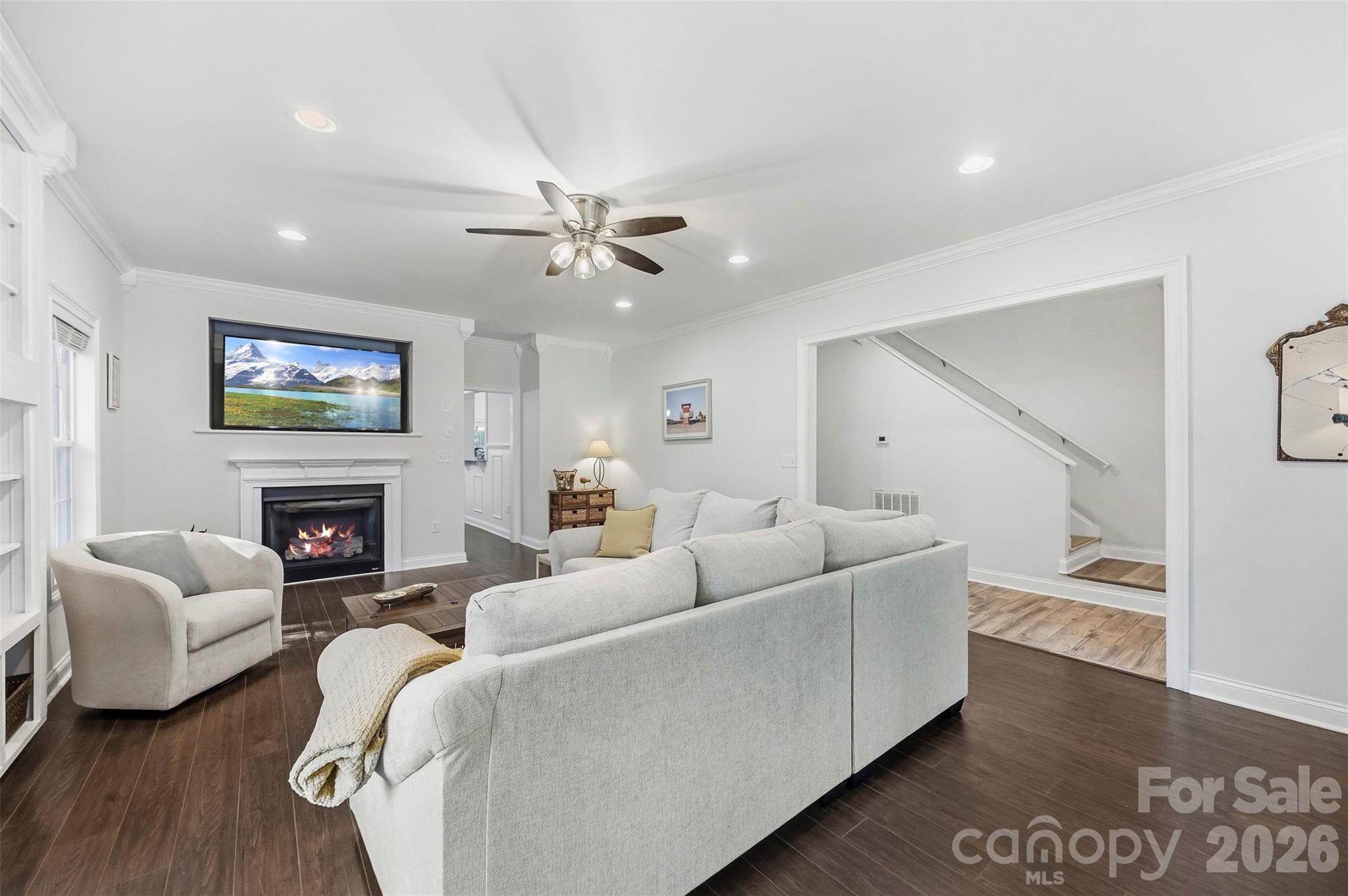 Living room with white sofas, a fireplace, and a staircase.