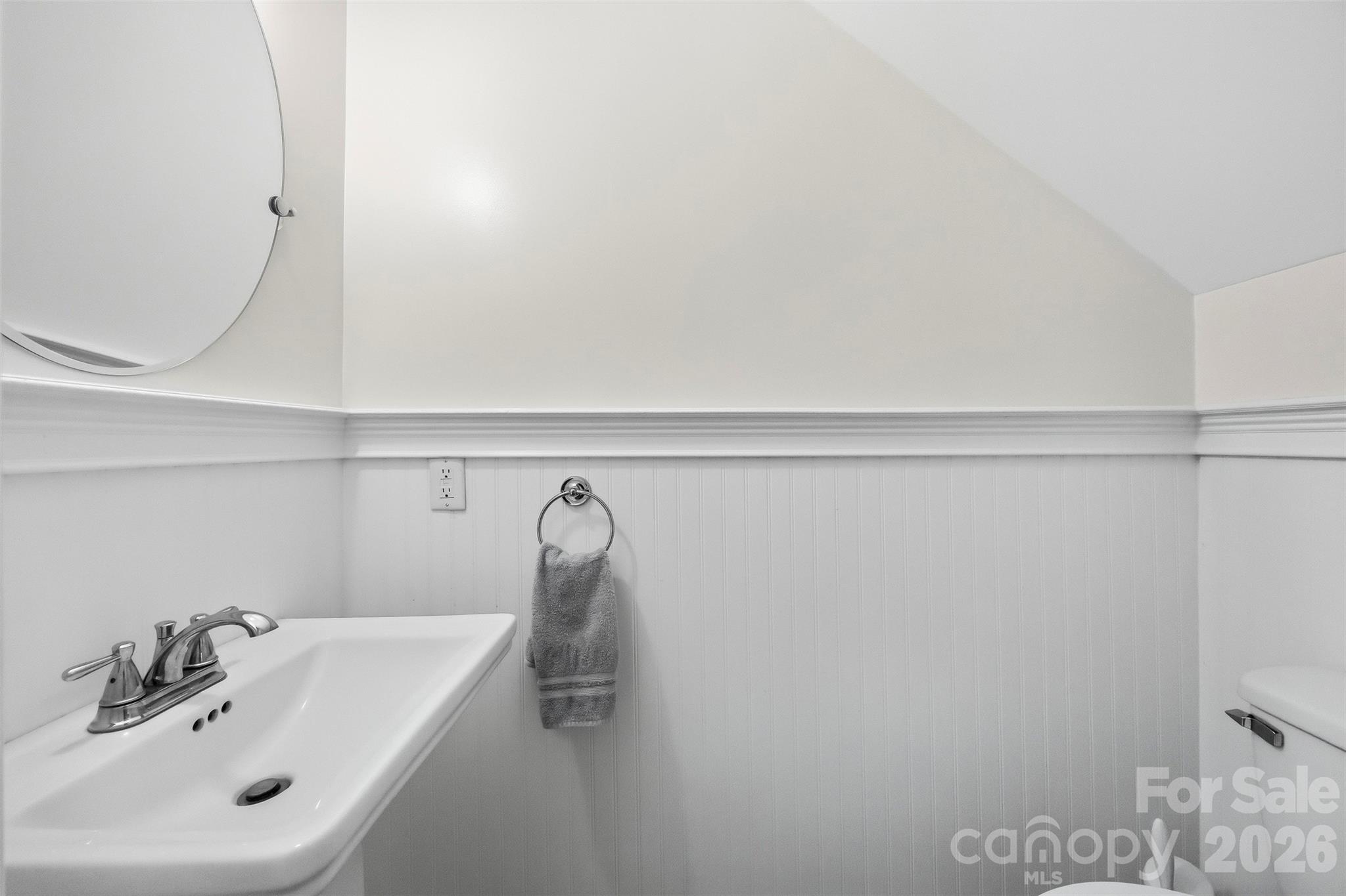 Bathroom vanity with a chrome faucet, round mirror, beadboard wainscoting, and towel ring.