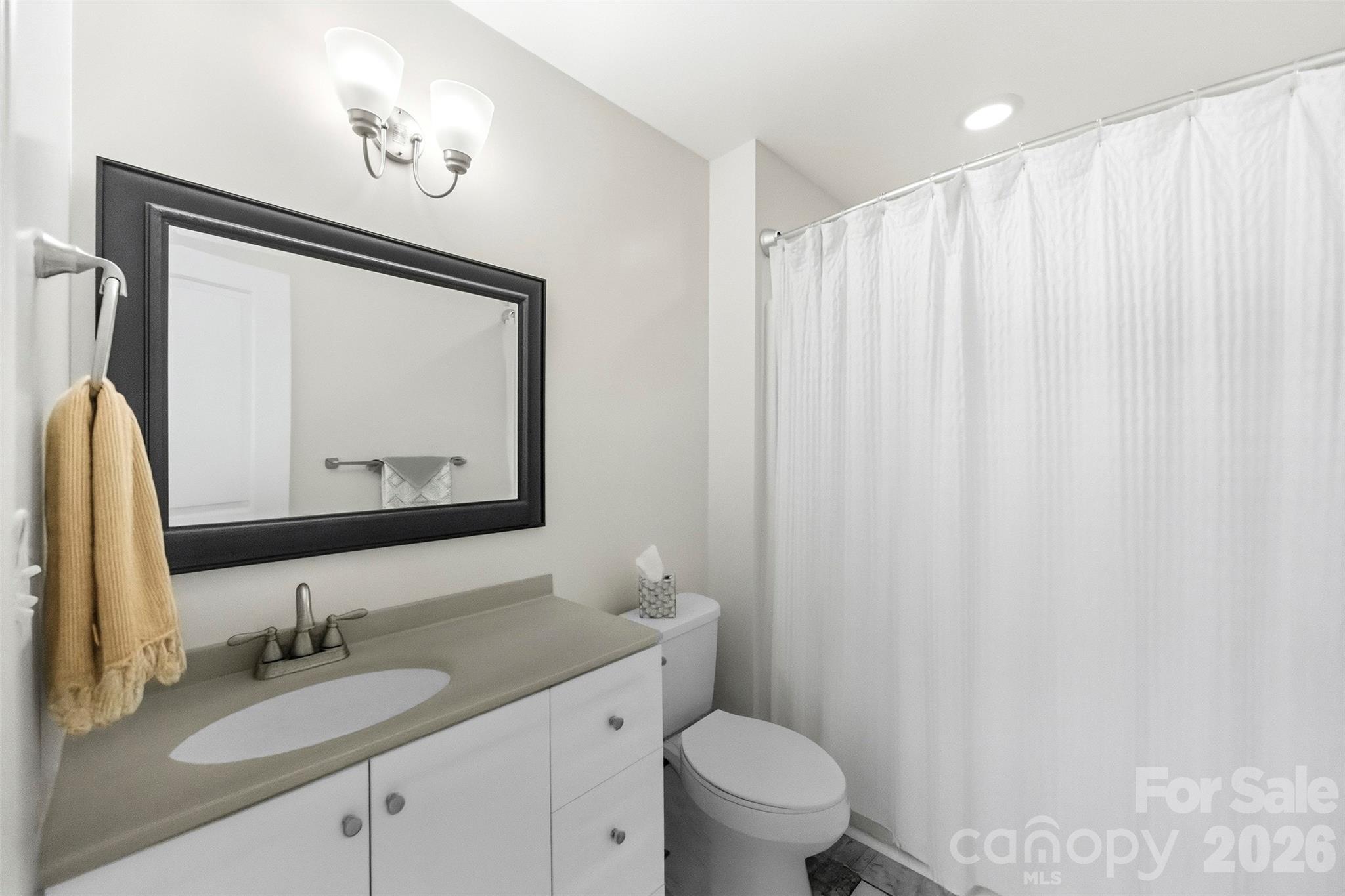 Bathroom with a white vanity, dark-framed mirror, toilet, and white shower curtain.