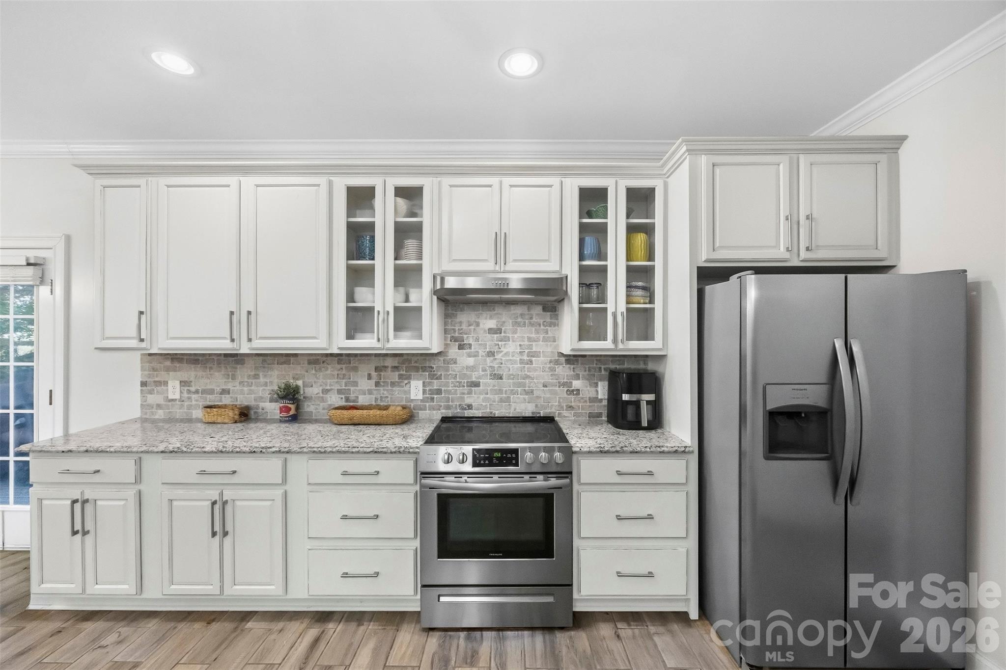 Kitchen with white cabinetry, gray brick backsplash, granite counters, and stainless steel appliances.