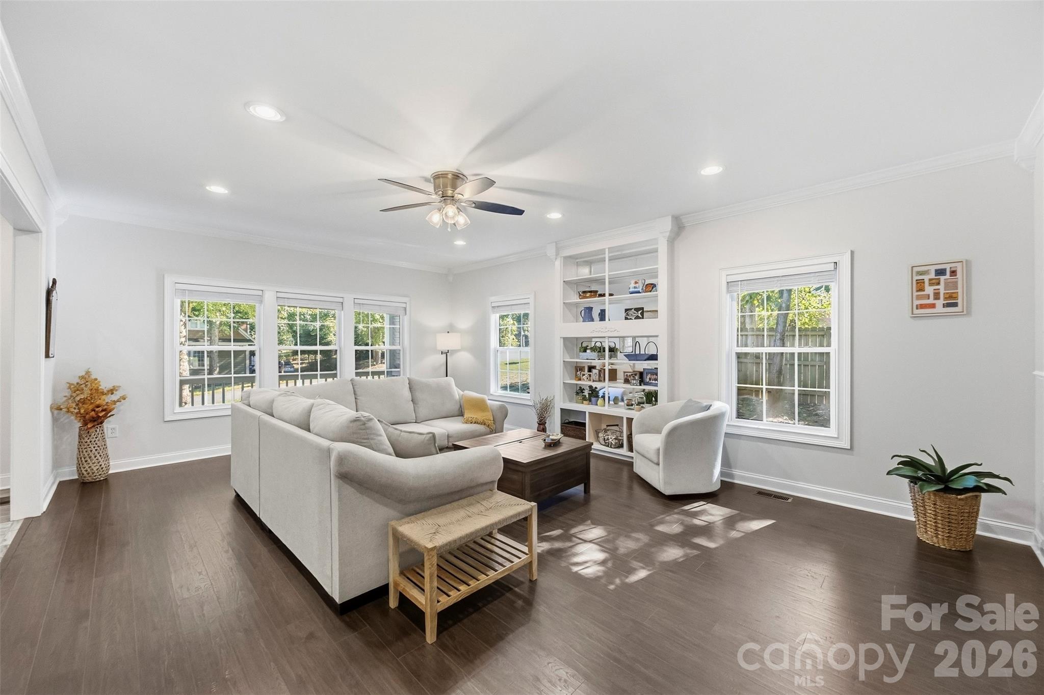 Furnished living room with a light gray sectional, built-in display shelves, and large windows.
