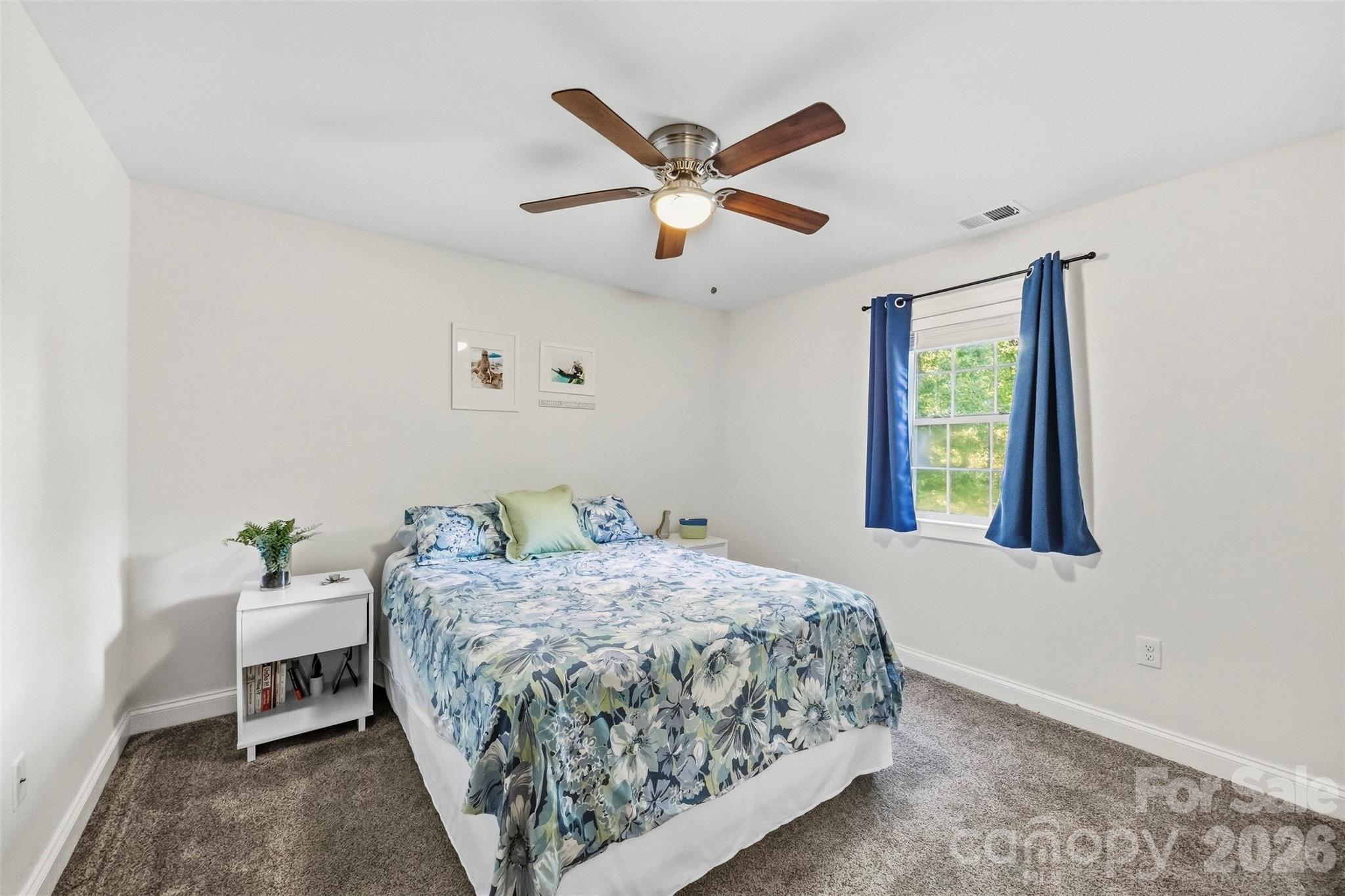 Bedroom with blue floral bedding, blue curtains, gray carpet, and a ceiling fan.