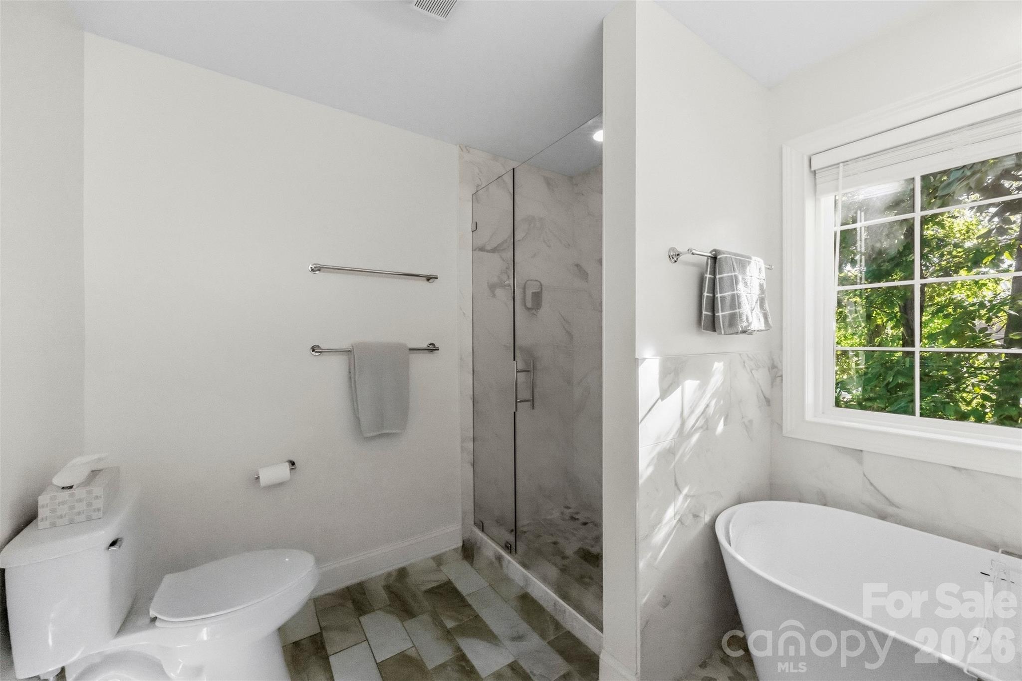 Bathroom with a glass shower and freestanding soaking tub beside a sunlit window.