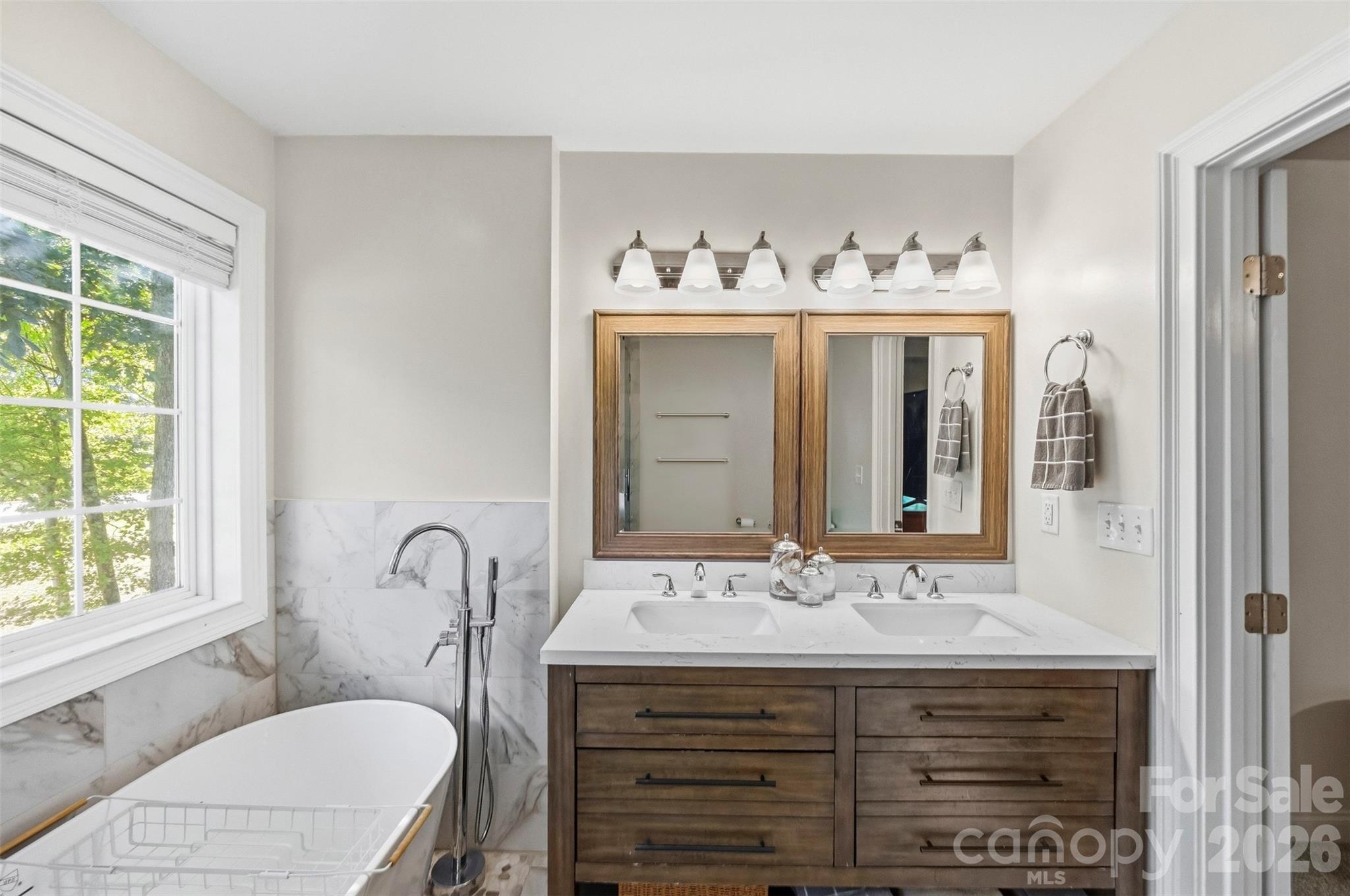 Bathroom with a freestanding soaking tub, marble-look tile, and wood double vanity with two sinks.