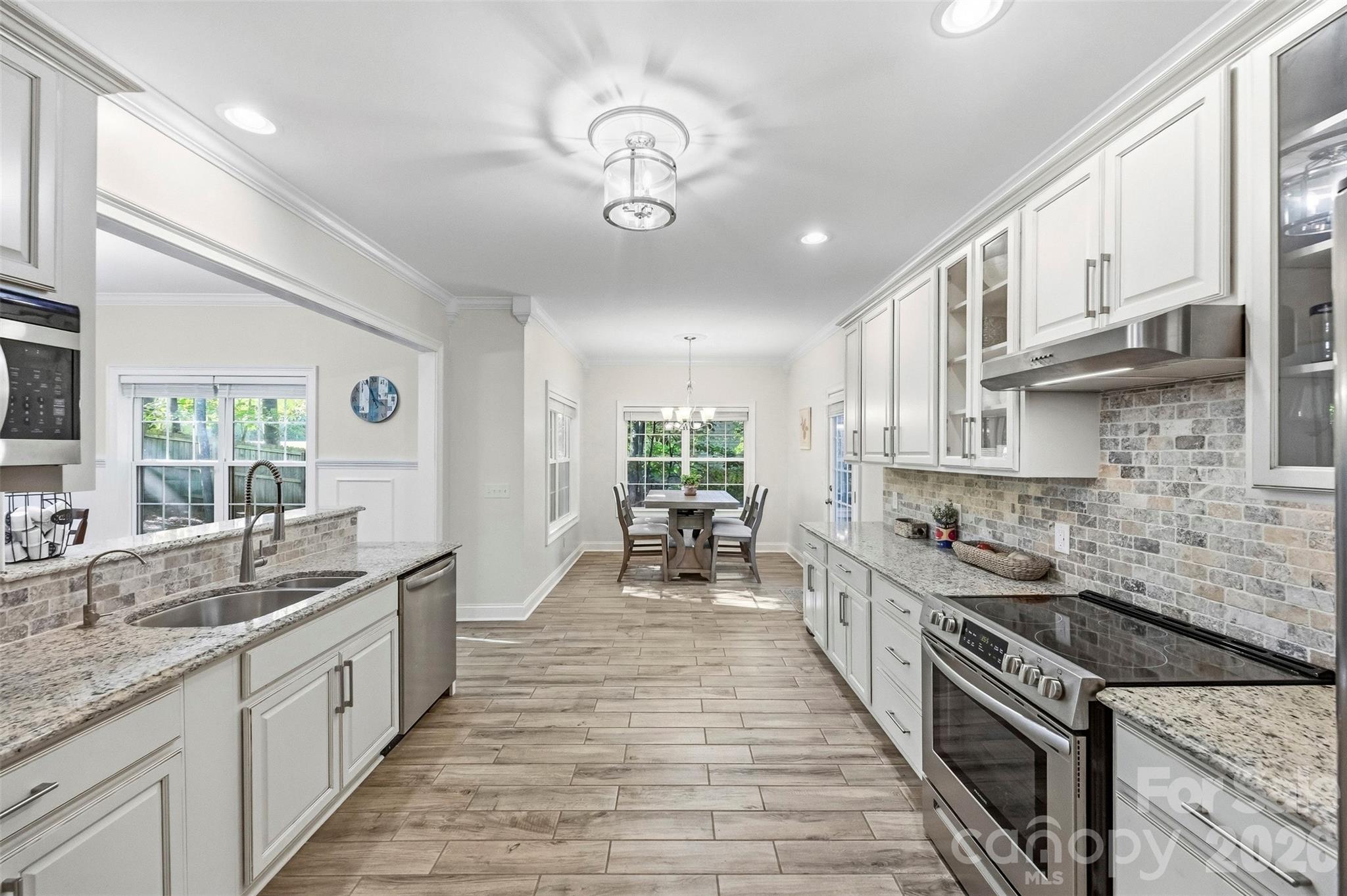 Bright white kitchen with granite counters and stone backsplash opening to a window-side dining area.