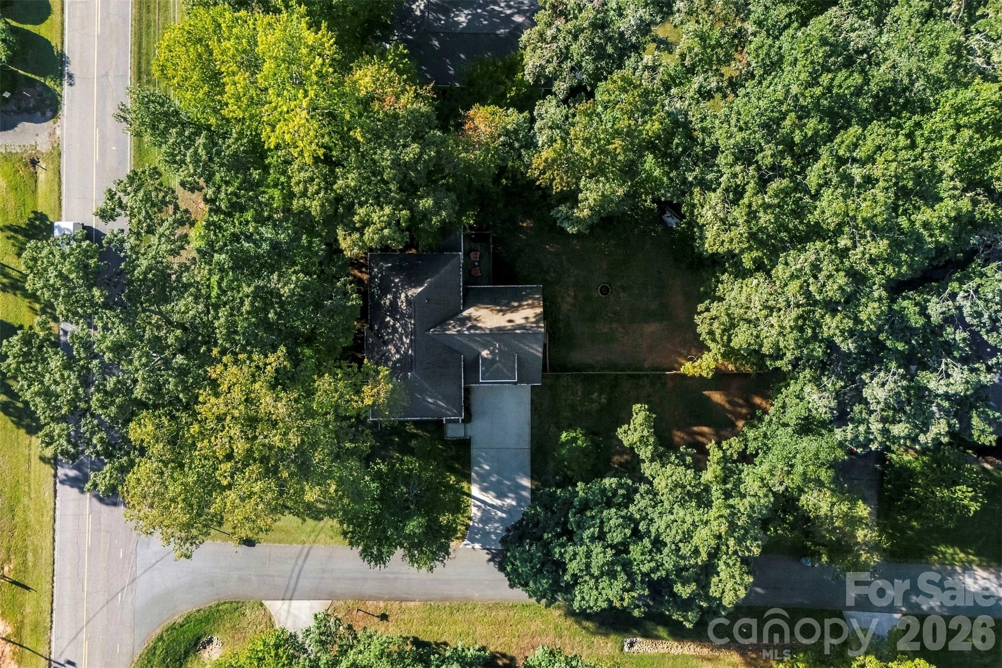 Aerial view of a home surrounded by mature trees, with a driveway and lawn.