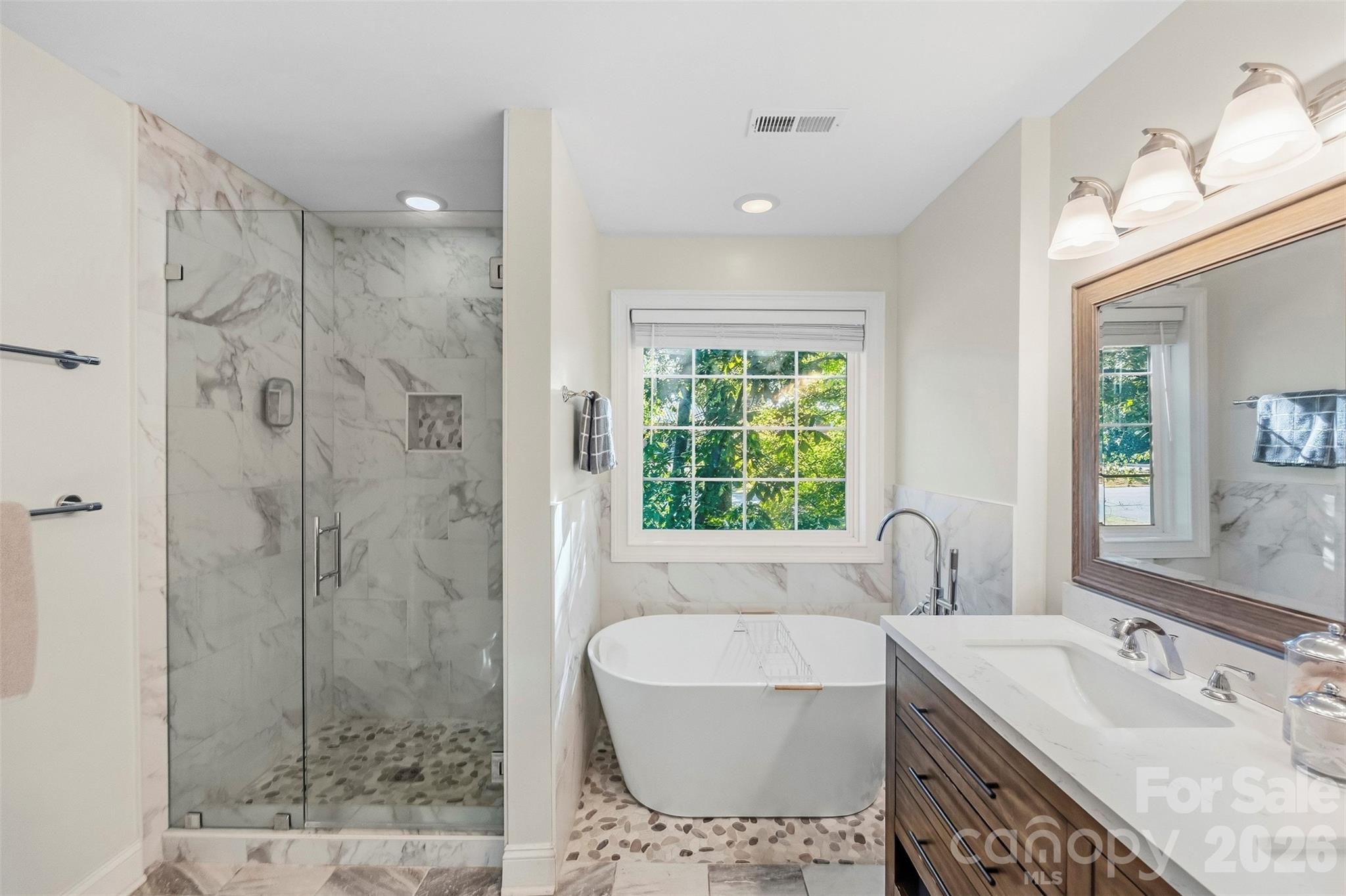 Bathroom with a marble-look walk-in shower, freestanding tub, pebble-tile floor, and double-sink vanity.