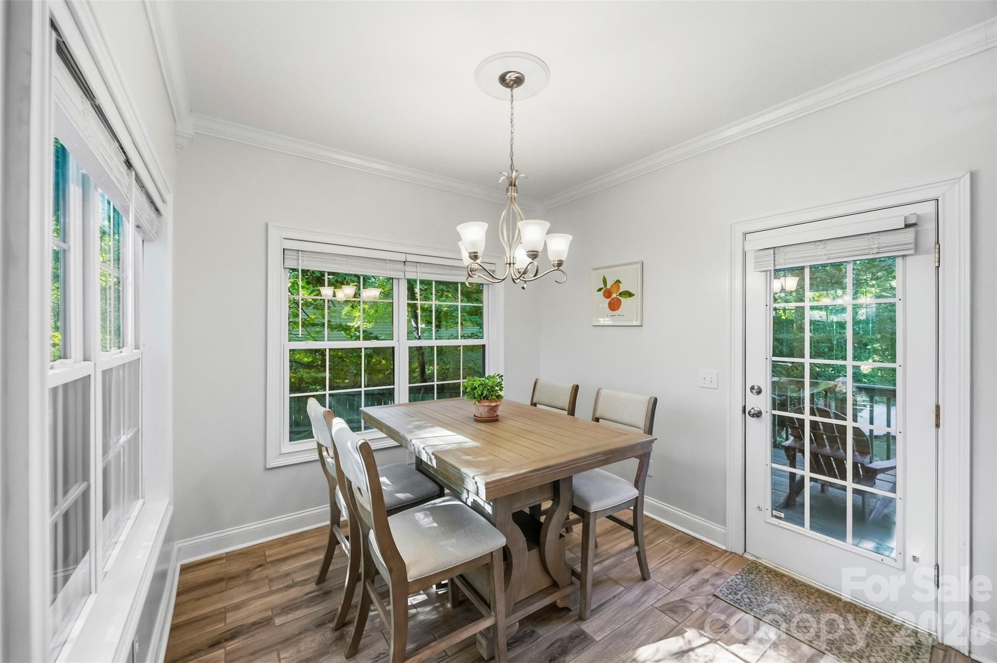 Dining room with a wooden table and chandelier, bright windows, and a glass door to the deck.