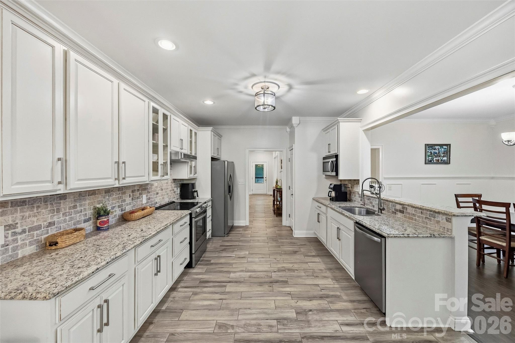 Kitchen with white cabinets, granite counters, stainless steel appliances, and a long breakfast bar.