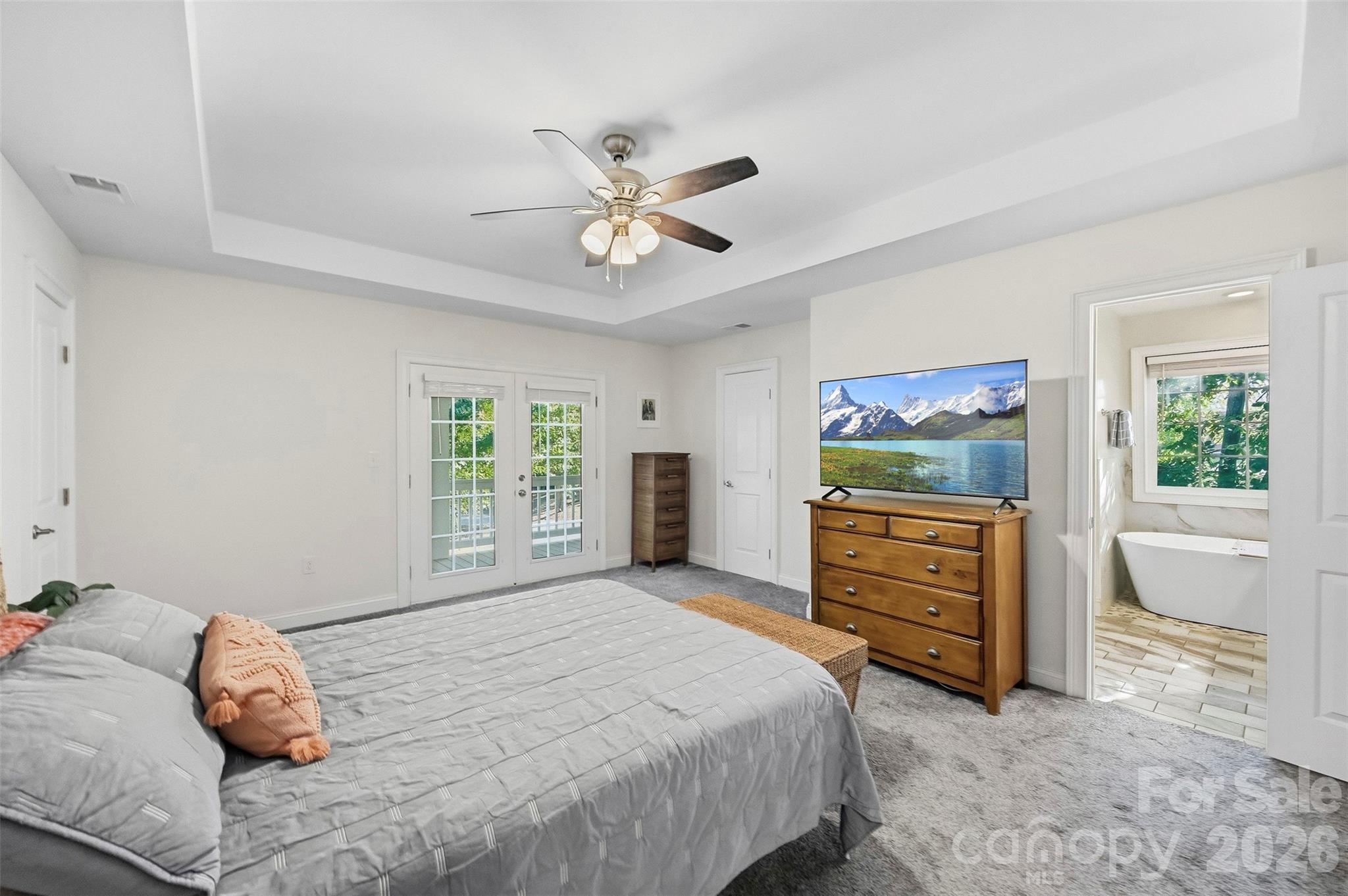 Furnished bedroom with French doors, a wooden dresser and TV, and an adjoining bathroom with a freestanding tub.