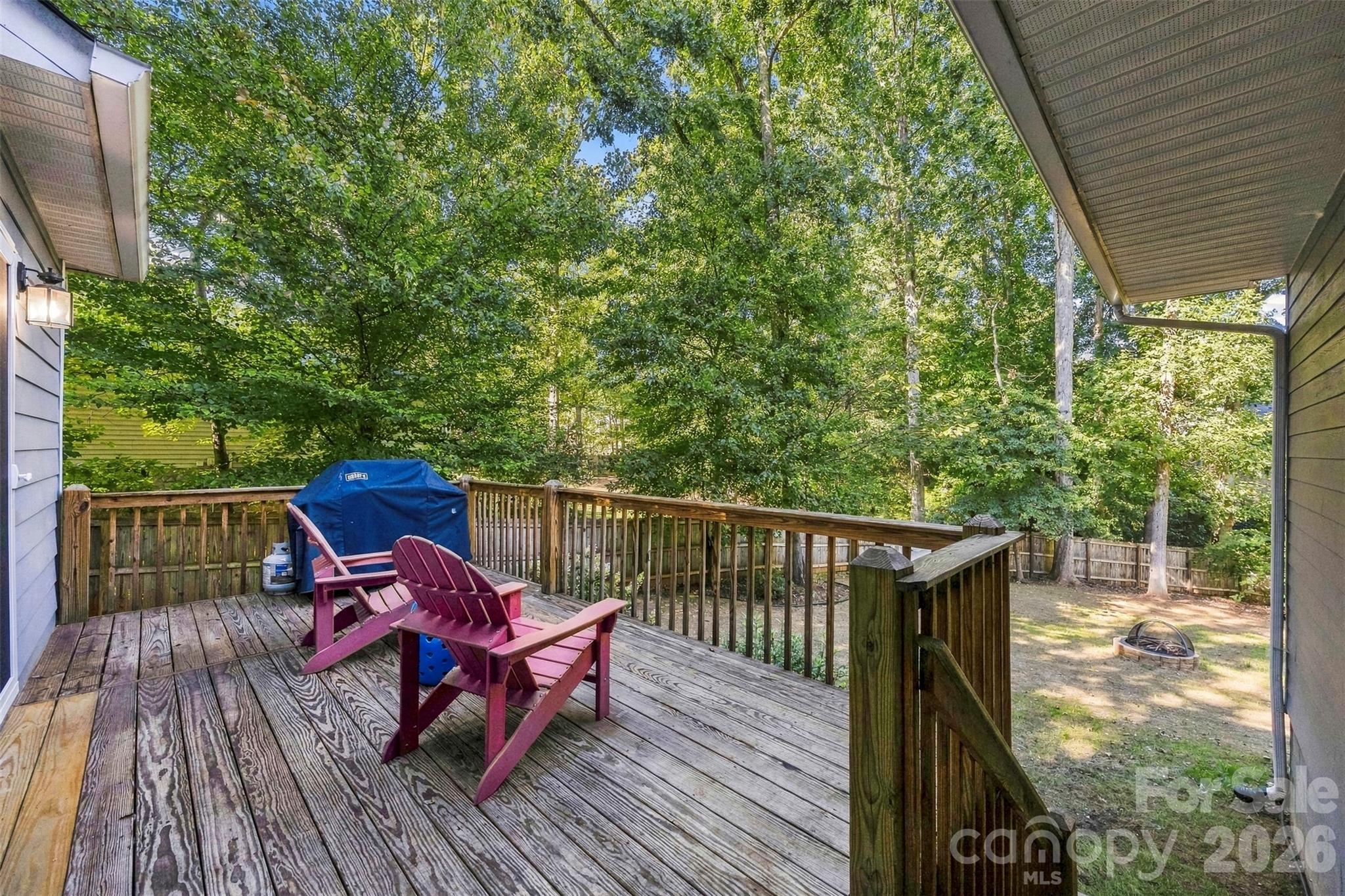 Wooden deck with magenta Adirondack chairs and a covered grill overlooking a leafy backyard.