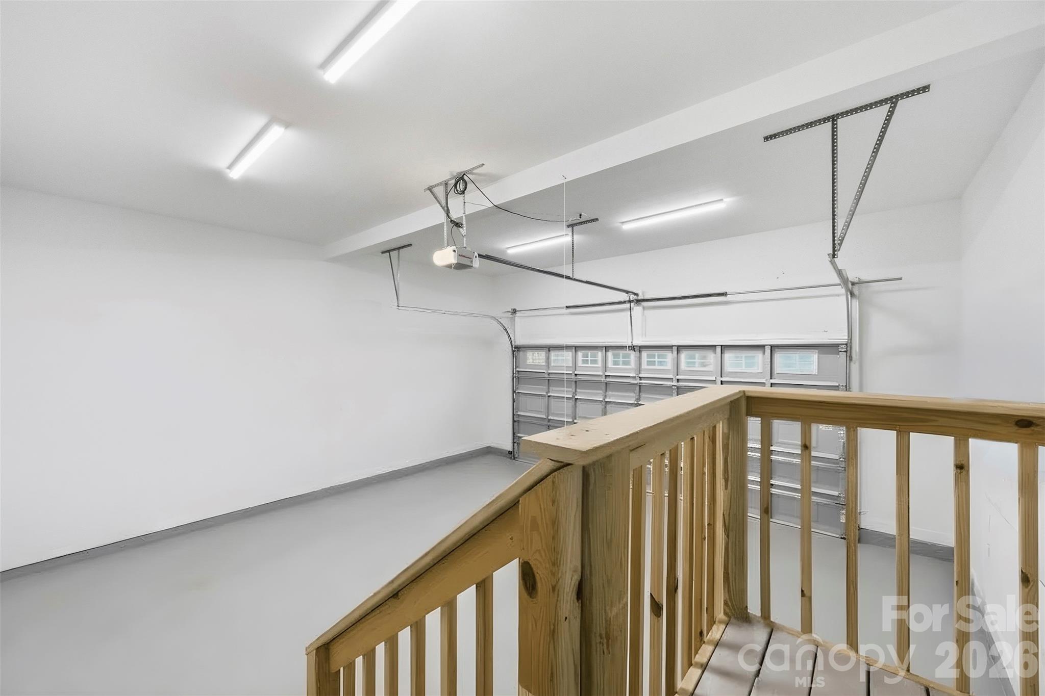 Empty garage with a sectional overhead door and unfinished wooden stair railing.