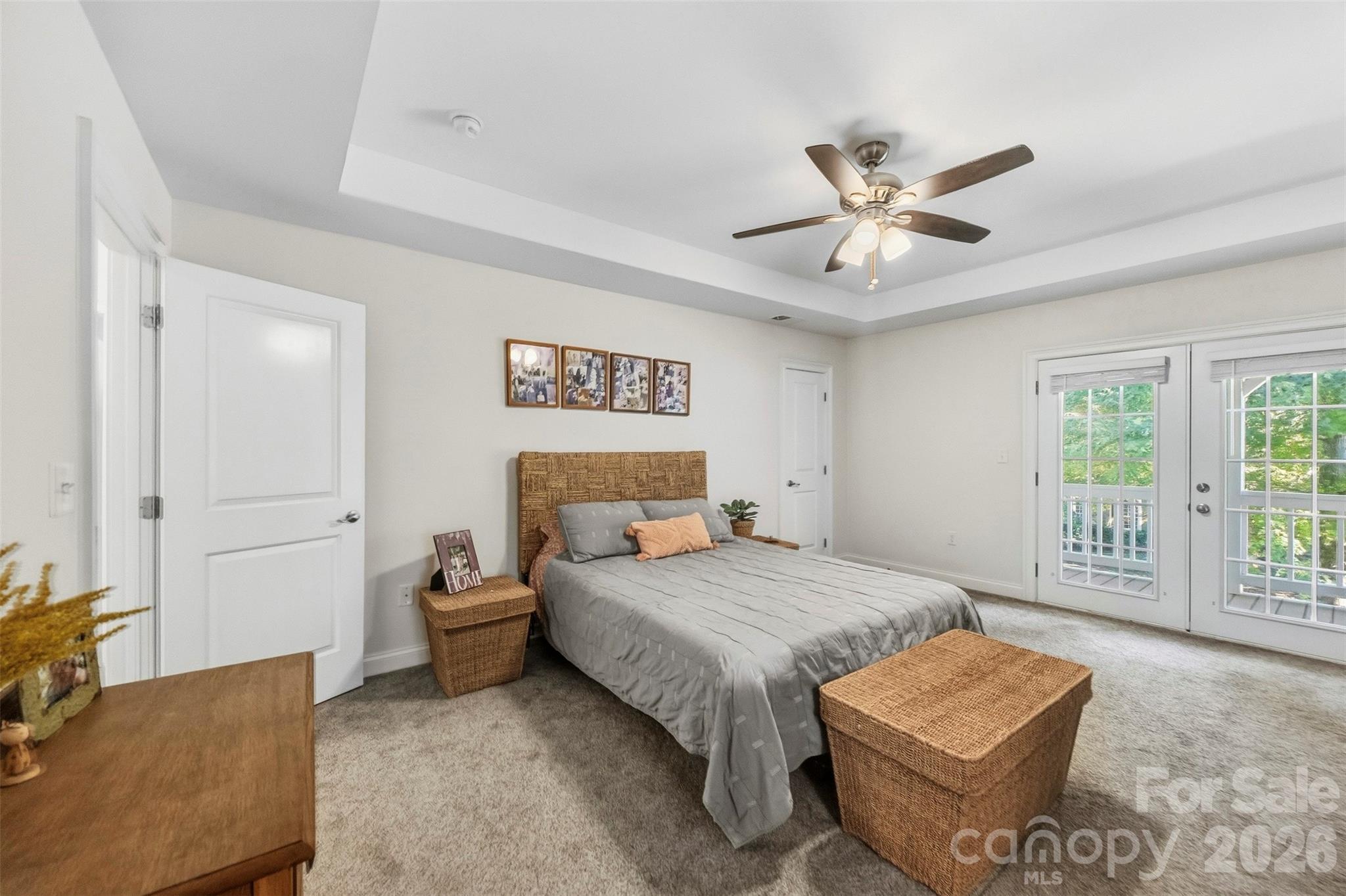 Furnished bedroom with a gray bed, woven headboard, tray ceiling, and glass doors to a balcony.