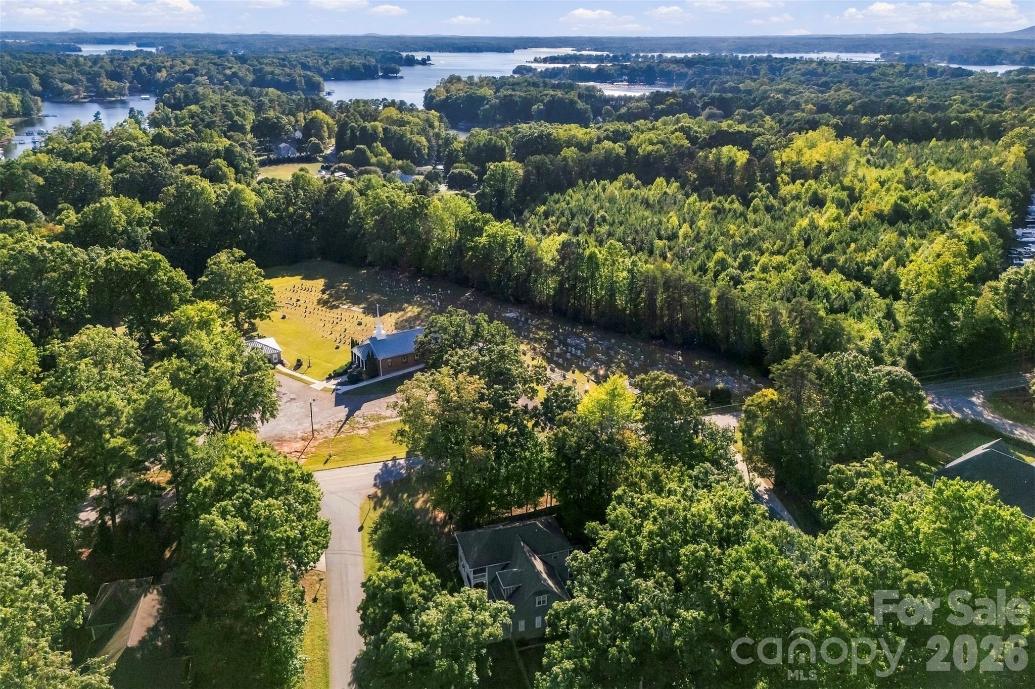Aerial view over wooded homes and a cemetery toward a broad lake.