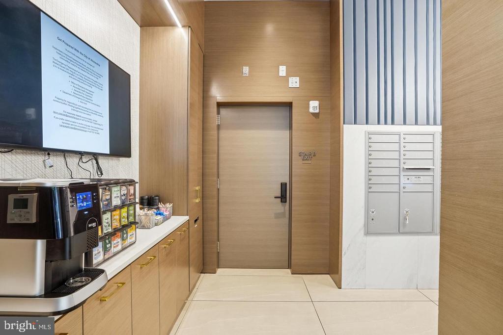 Building lobby with a coffee station, mailboxes, and a wood-paneled stairwell door.