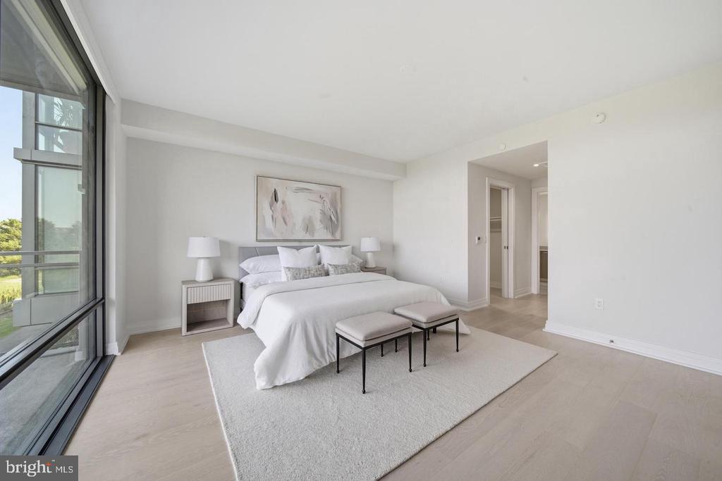 Staged bedroom with a white bed, two upholstered benches, and floor-to-ceiling windows.