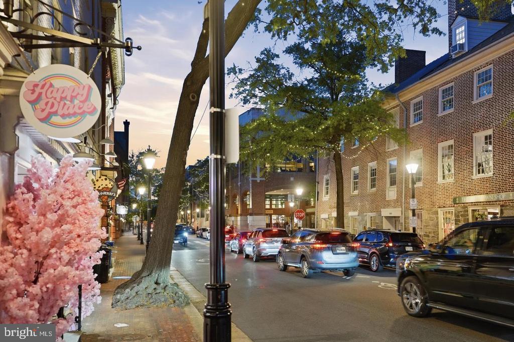 Alexandria street at dusk, with brick storefronts, parked cars, and a lit Happy Place sign.