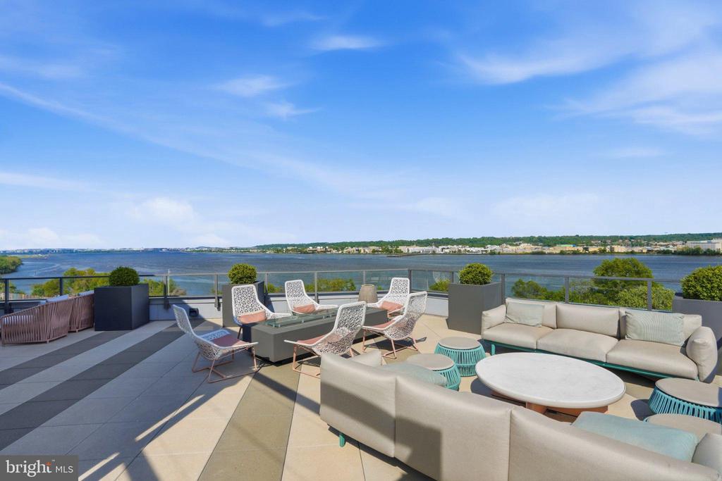 Rooftop terrace with modern lounge seating and planters overlooking the water.