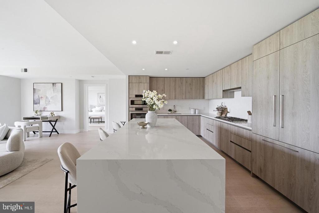 Open-plan kitchen with a large white island, light wood cabinetry, and built-in ovens.