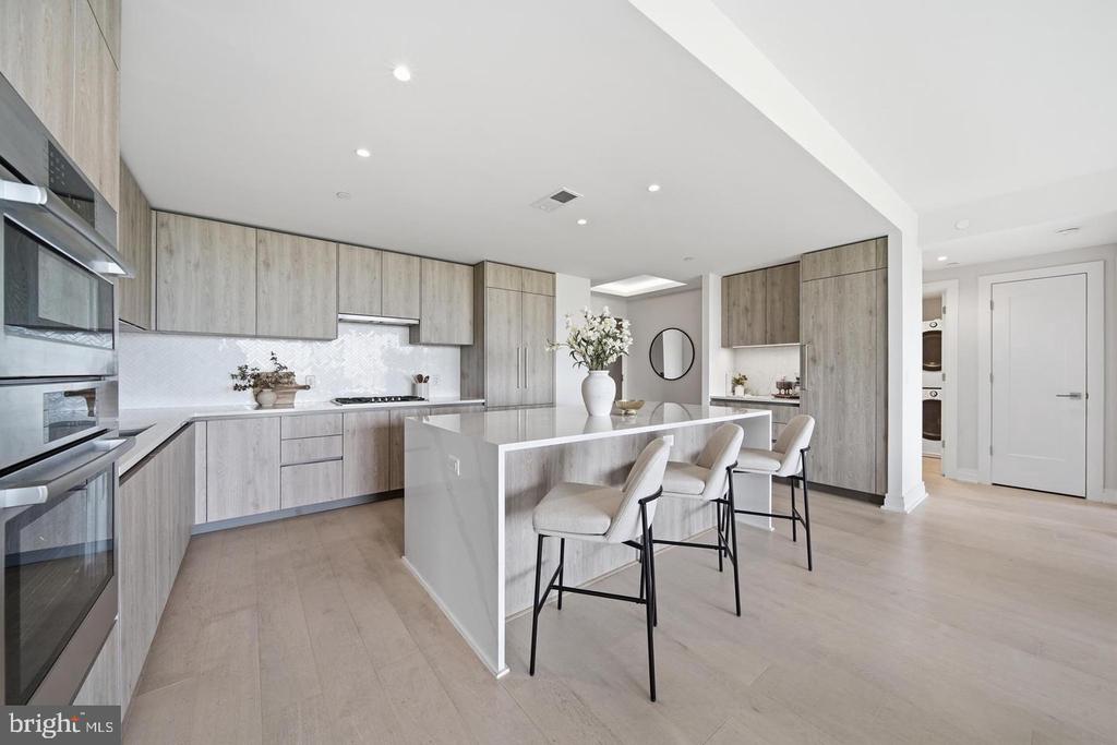 Modern kitchen with a white island, light wood cabinets, and three upholstered bar stools.