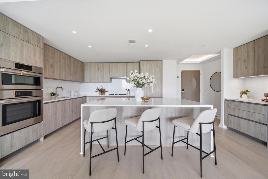 Modern condo kitchen with a white island, three bar stools, and light wood cabinetry.