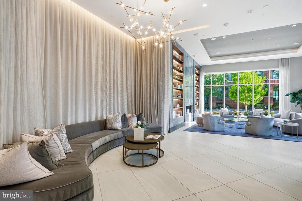Modern residential lounge with curved gray sofas, a statement chandelier, and large windows overlooking a leafy courtyard.