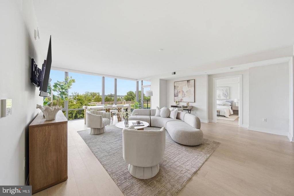 Bright living room with a curved white sectional and floor-to-ceiling windows overlooking greenery.