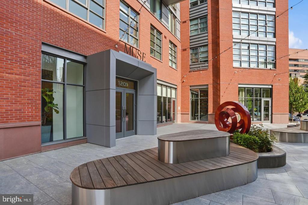 MUSE condominium entrance with red brick facade, sculptural seating, and a red abstract sculpture.