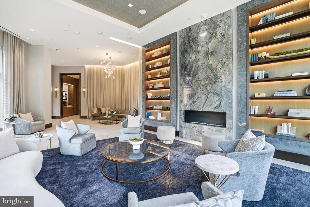Furnished condominium lounge with a marble fireplace wall and illuminated built-in shelves.
