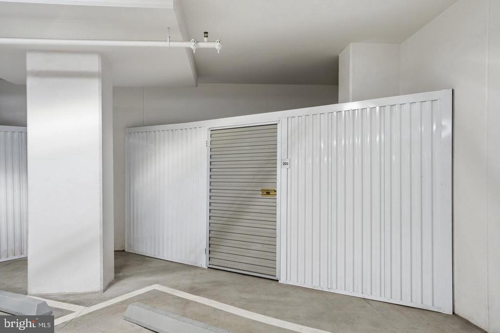 A white metal storage unit with a roll-up door in a concrete garage.