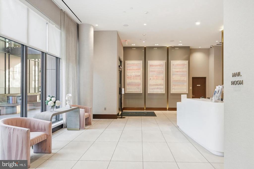 Condominium lobby with a white reception desk, blush seating, tall windows, and mail room sign.