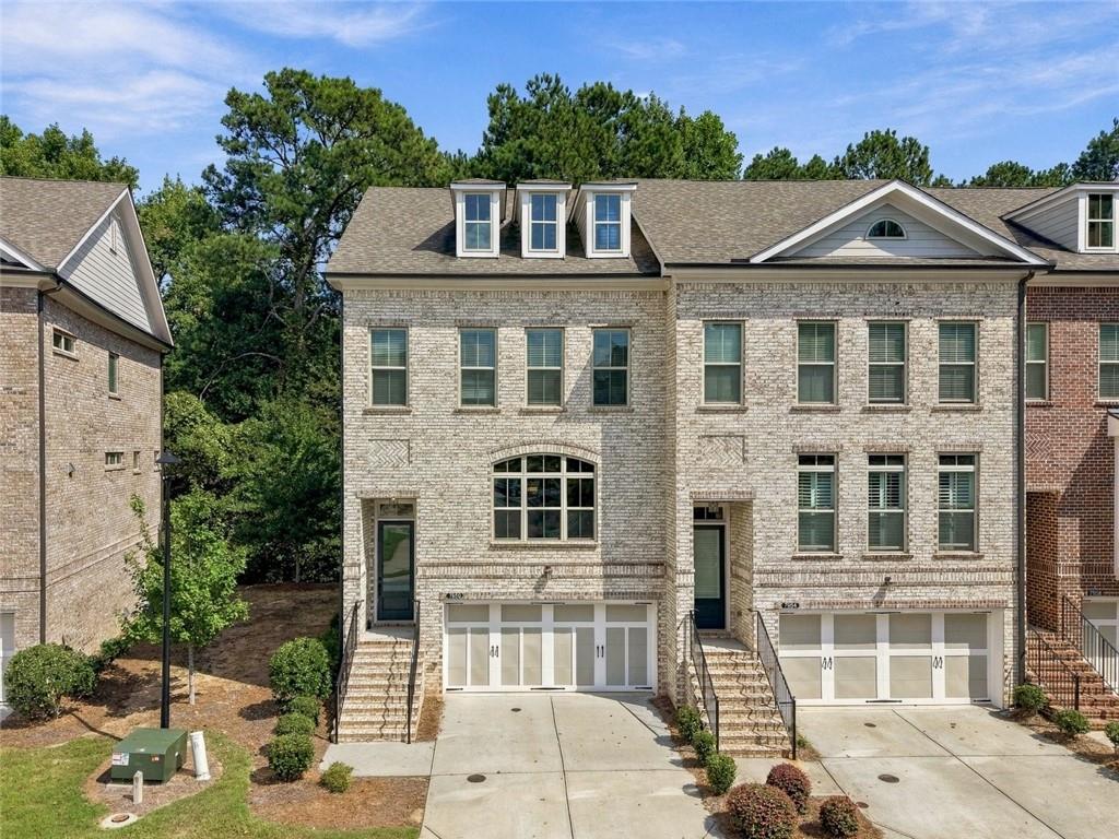 Light-brick townhomes with dormer windows, attached garages, and concrete driveways.