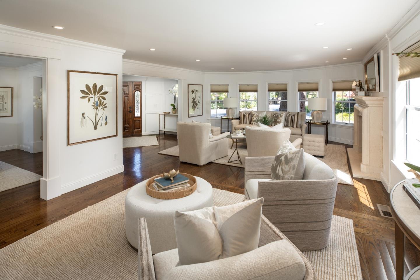 Furnished living room with a white fireplace, botanical artwork, and large windows.