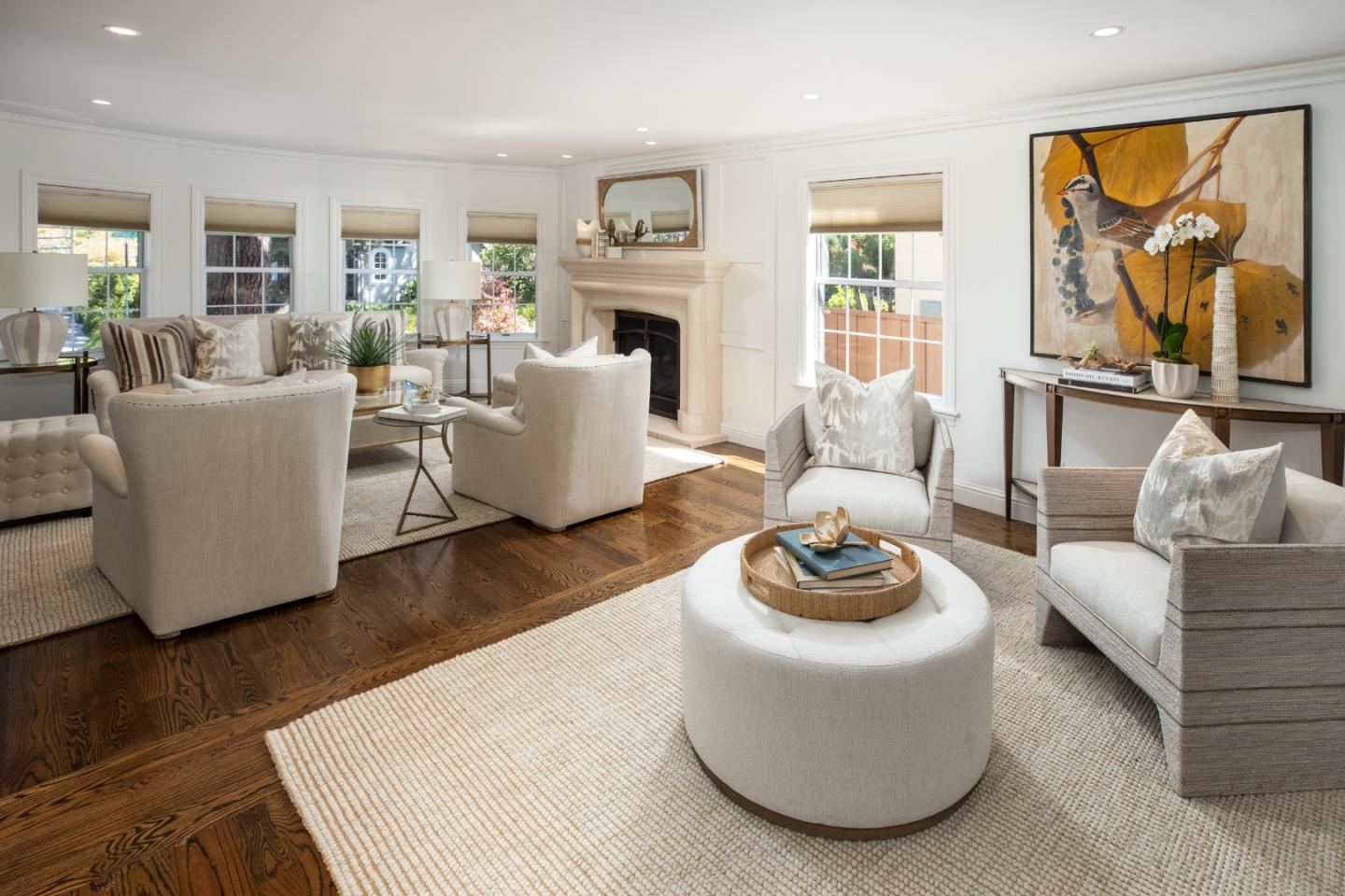Staged living room with a fireplace, white seating, large windows, and dark hardwood floors.