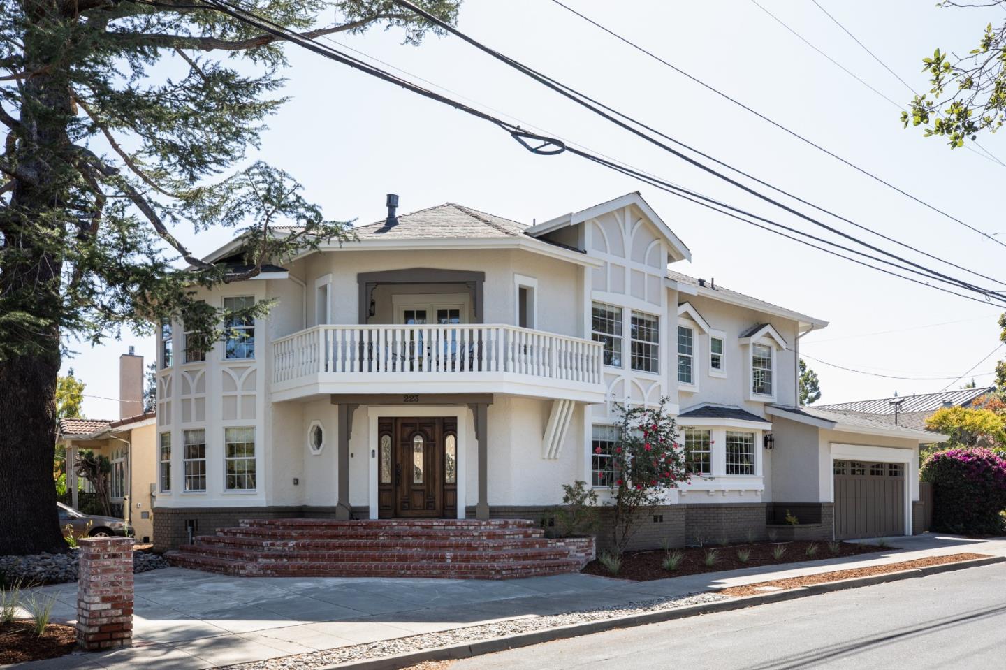 Two-story white house with a broad balcony, decorative gables, brick steps, and attached garage.