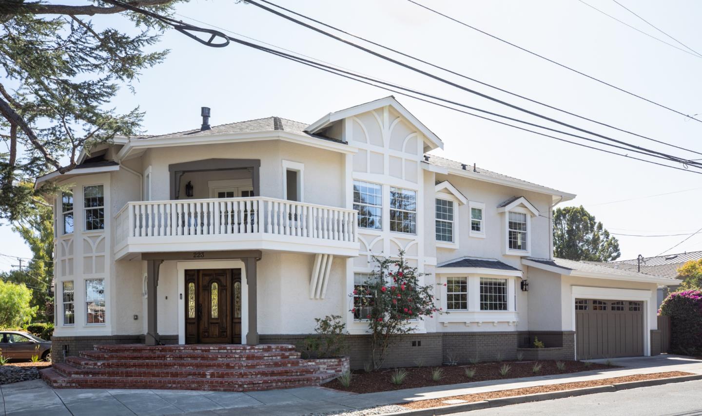 Two-story cream home with a white-trimmed balcony, brick steps, and attached garage.