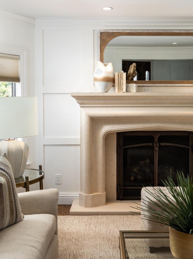 Living room with a cream stone fireplace, ornate mantel mirror, neutral sofa, and potted plant.