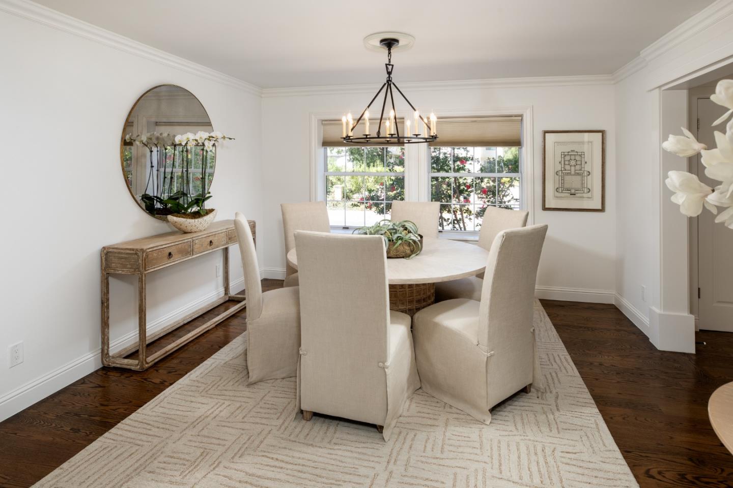 Dining room with a round table, upholstered chairs, chandelier, and large garden-facing windows.