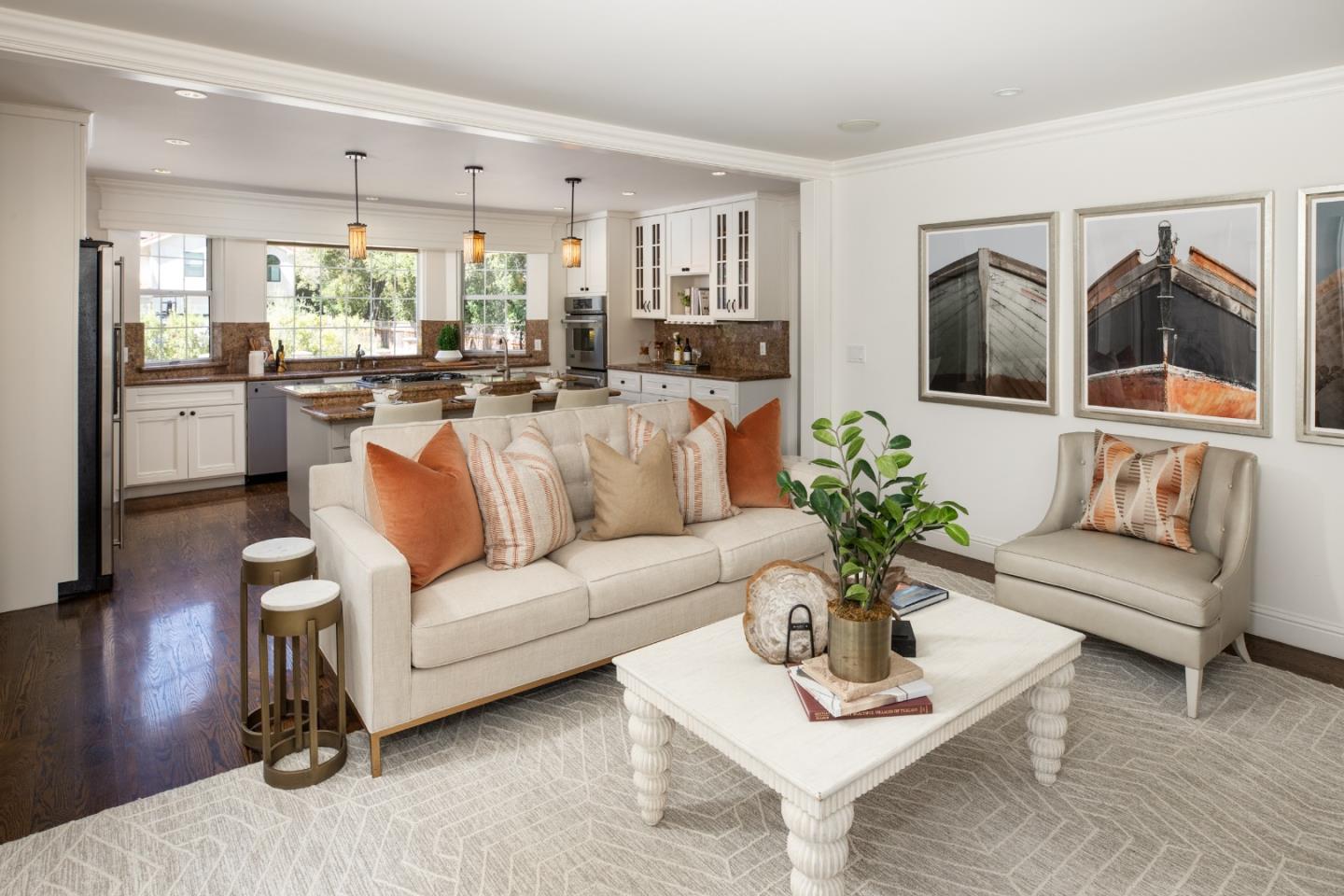 Staged living room with a cream sofa, white coffee table, framed boat prints, and an open kitchen.