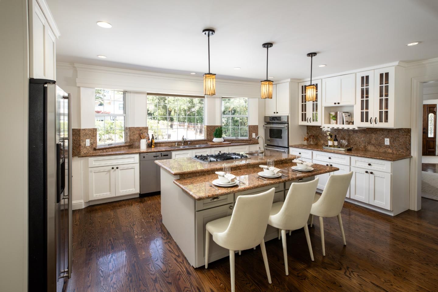 Kitchen with a large stone-topped island, white cabinetry, stainless steel appliances, and dark hardwood floors.