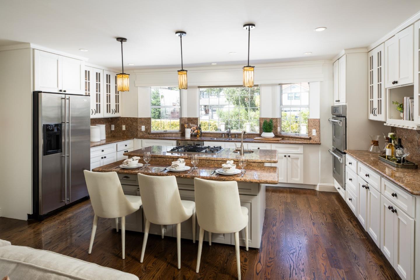 Bright kitchen with a stone island, white cabinets, stainless steel appliances, and dark wood floors.