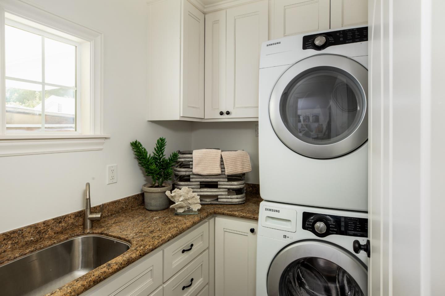 Laundry room with stacked washer and dryer beside a stainless-steel sink and stone countertop.