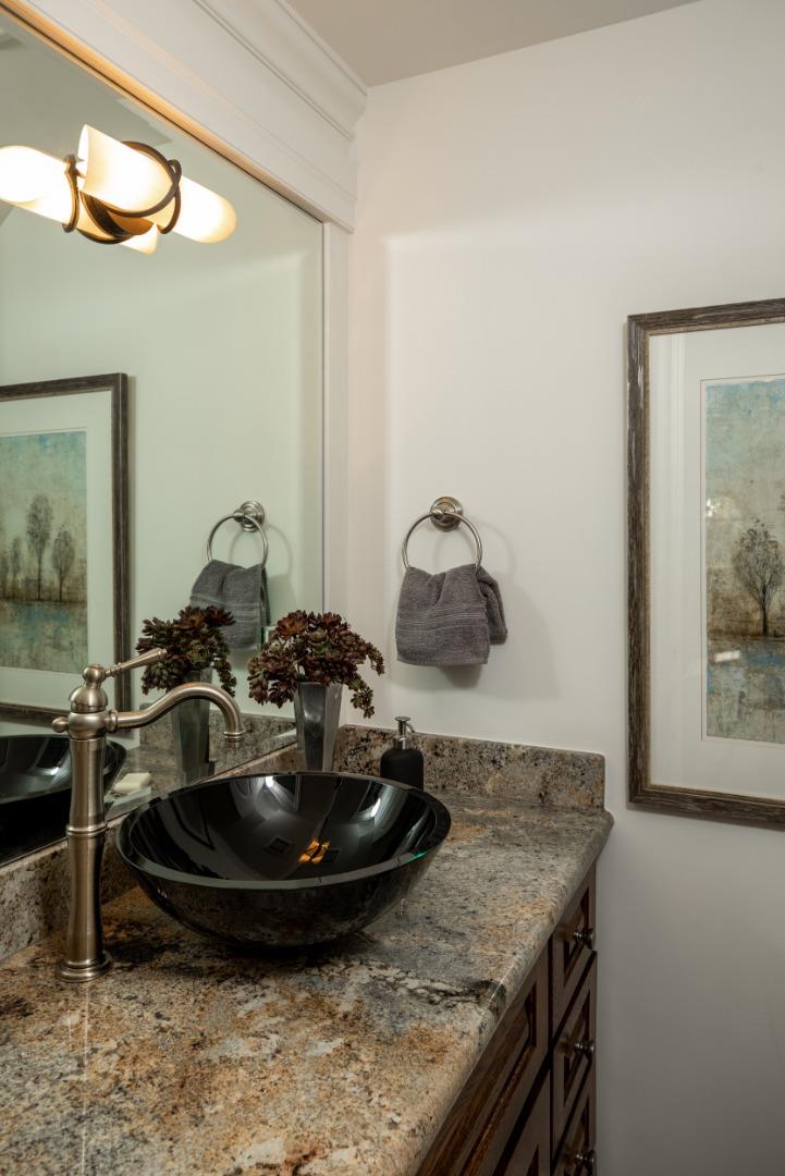 Bathroom vanity with a black vessel sink, stone countertop, bronze faucet, and framed artwork.