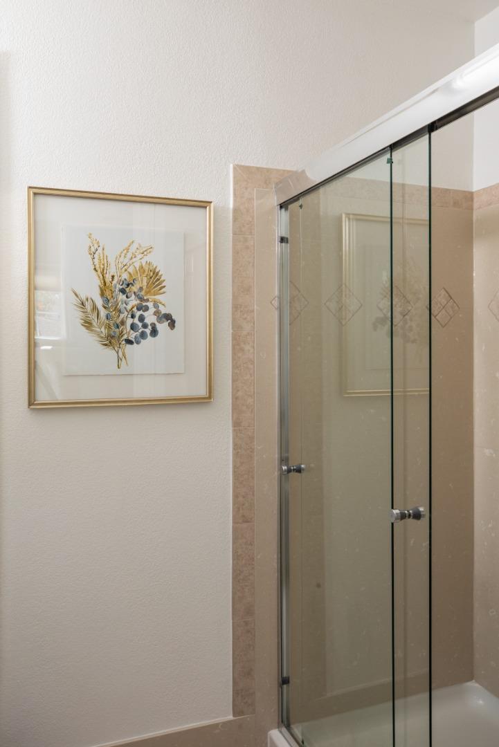 Bathroom shower with glass doors, beige tile, and framed botanical artwork.