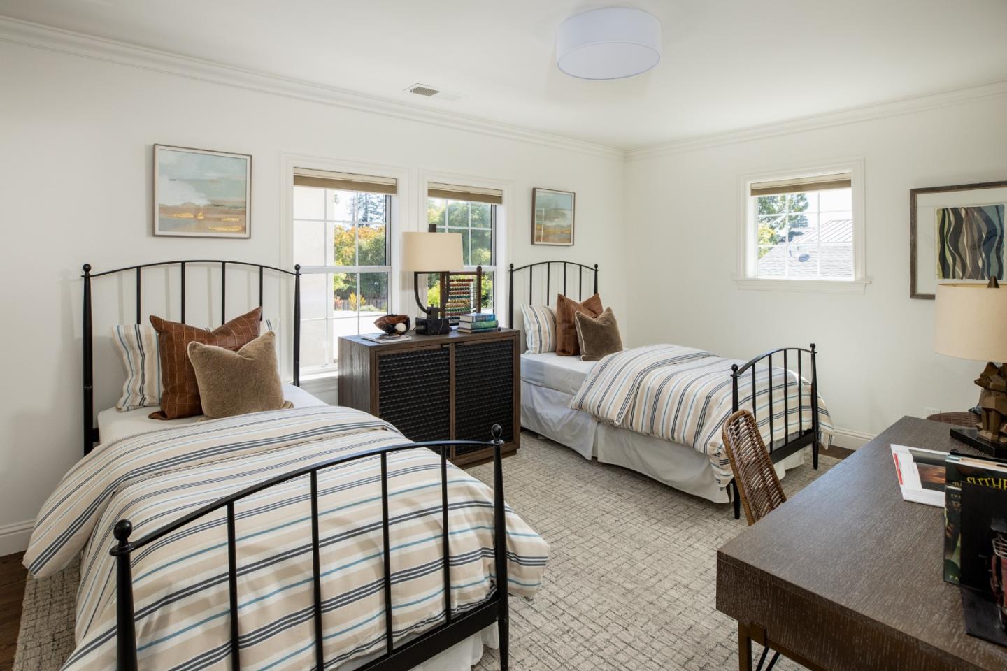 Staged bedroom with two black metal twin beds and striped bedding beside bright windows.