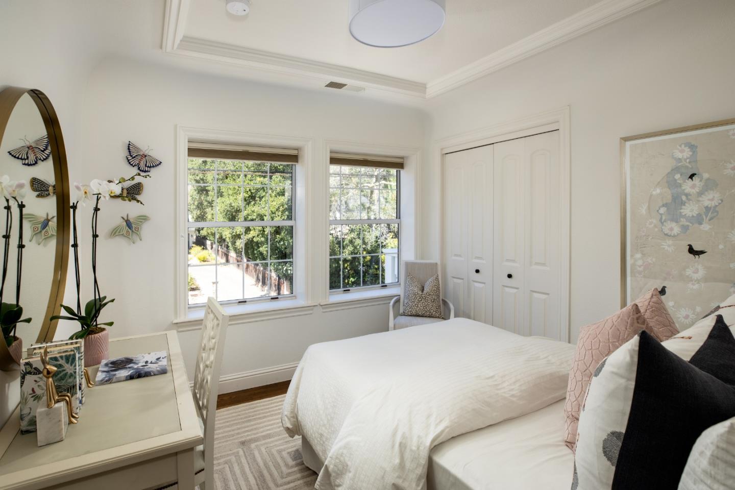 Furnished bedroom with a white bed, two large windows, and a vanity.