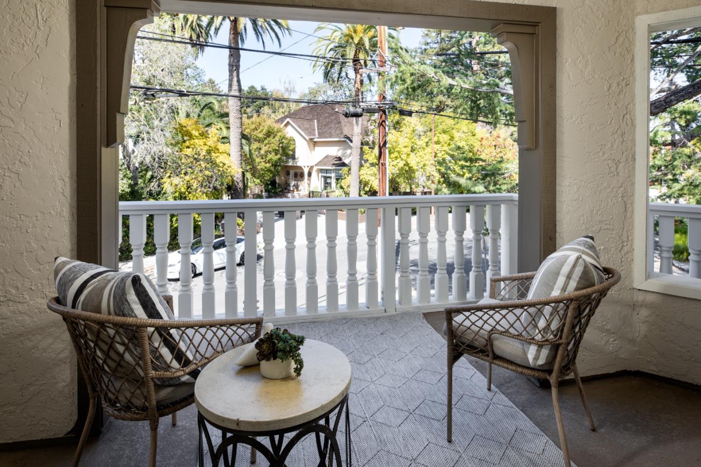 Covered porch with wicker chairs and a view of leafy trees and neighboring homes.