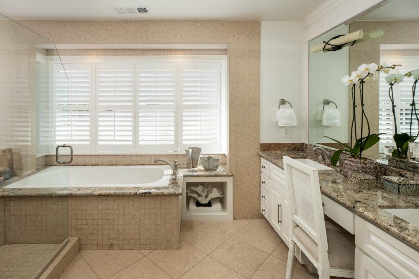 Bathroom with a soaking tub beneath plantation shutters and a granite vanity.